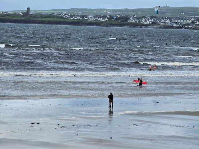 kite surfer in action, as a few dippers enter the water and two surfers departs